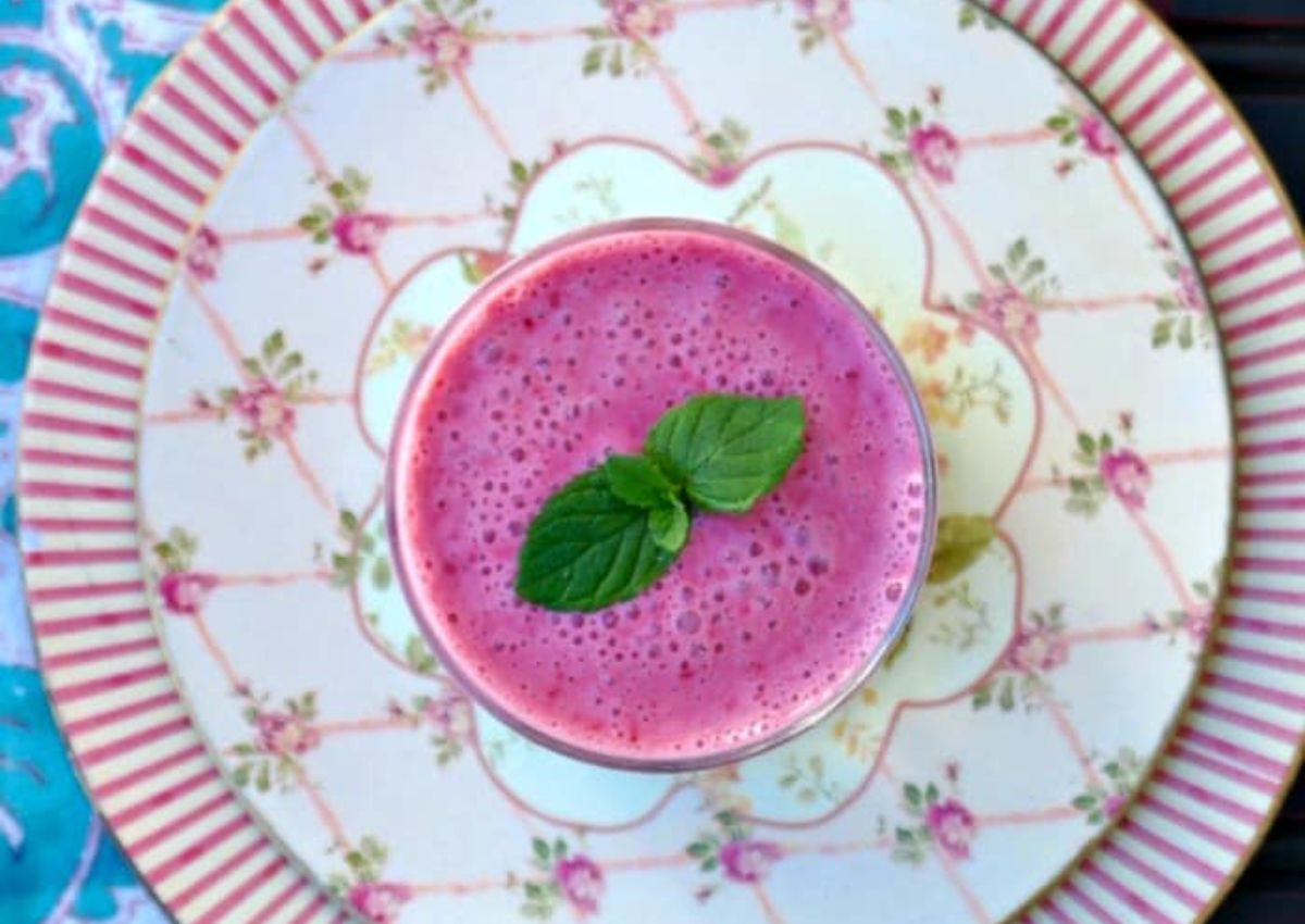 A pink smoothie topped with two mint leaves sits on a decorative plate with floral and striped patterns, viewed from above.
