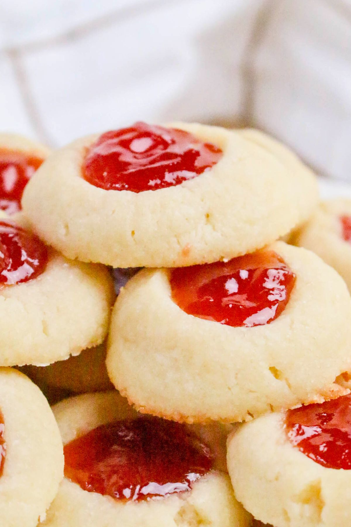 A close-up of several thumbprint cookies with red jam filling in the center, stacked on top of each other.