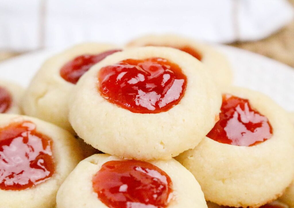 A plate of round thumbprint cookies filled with glossy red jam in the center.