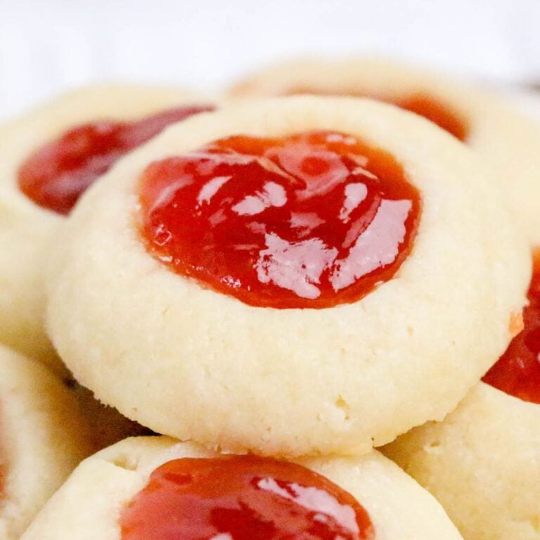 Close-up of stacked thumbprint cookies with a dollop of bright red jam in the center of each cookie.