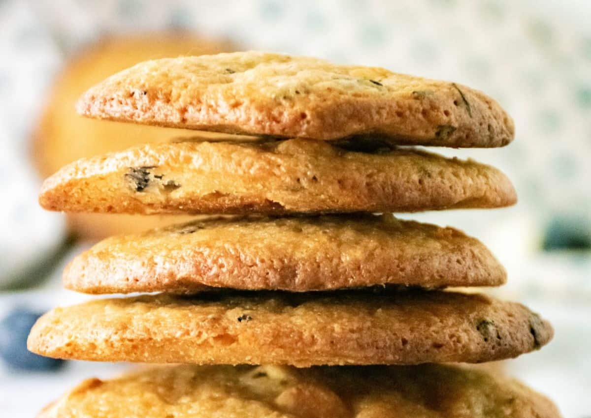 A close-up of a stack of four golden-brown cookies with visible chocolate chips on a blurred background.