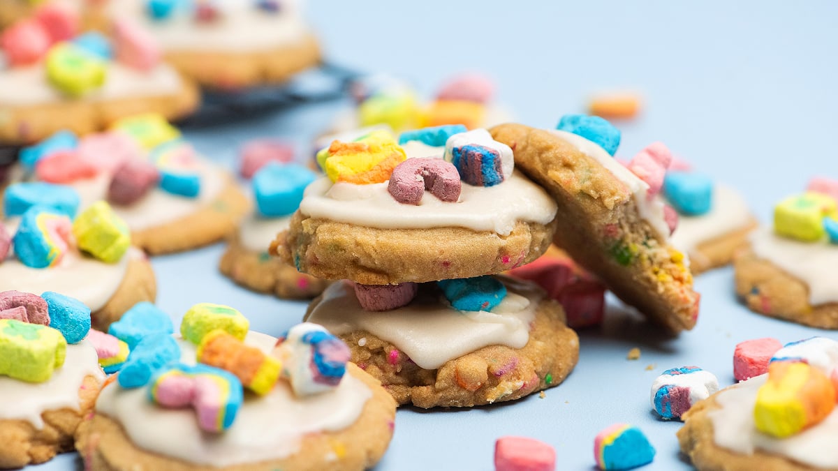 Cookies topped with white icing and colorful cereal marshmallows are arranged on a light blue surface.