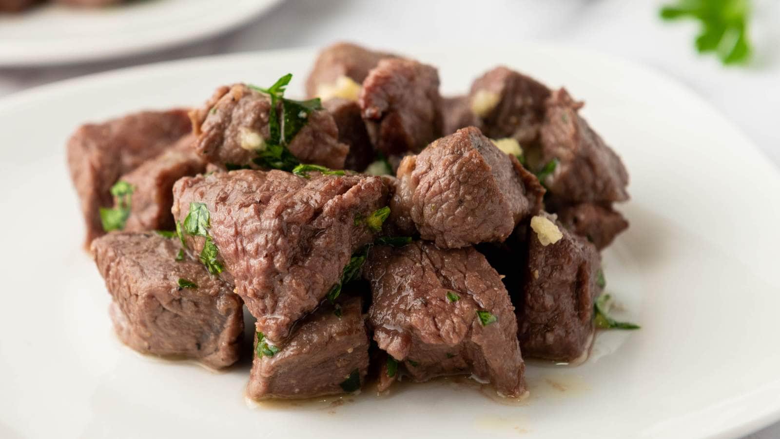 Chunks of cooked beef garnished with chopped herbs are arranged on a white plate.