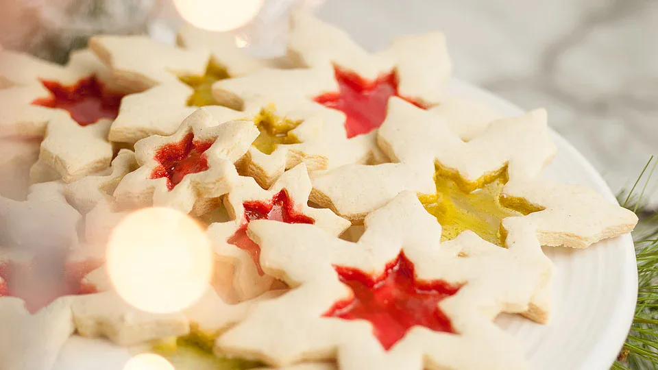 A plate of star-shaped cookies with translucent red and yellow centers, arranged in a pile on a white dish.