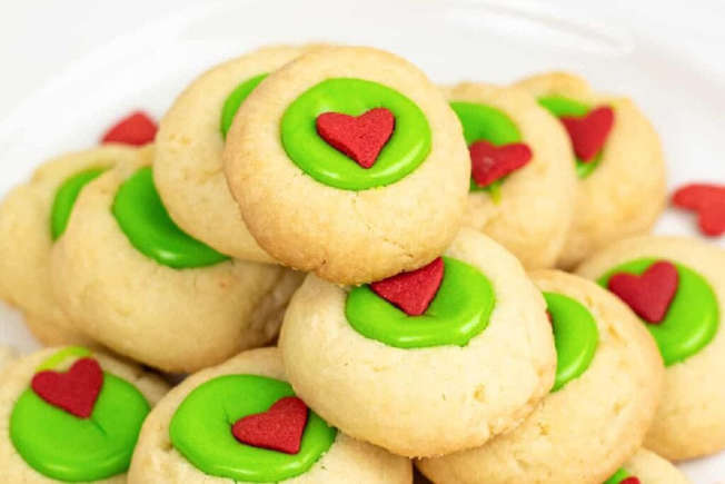 A plate of round sugar cookies topped with green icing and a small red heart-shaped decoration in the center of each cookie.