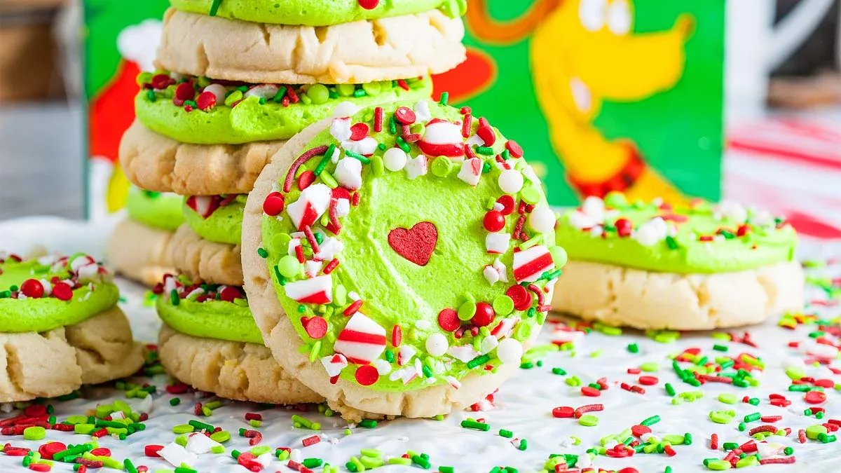 A stack of sugar cookies with green frosting, red heart decorations, and festive red, white, and green sprinkles, arranged on a white surface.