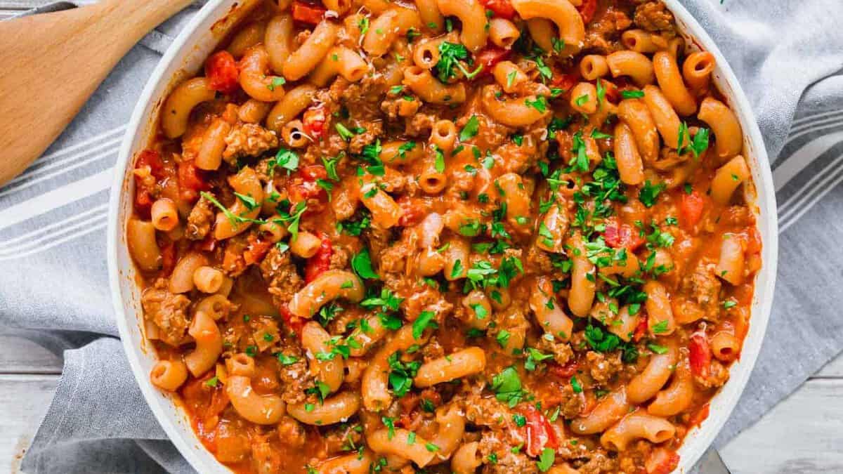 A skillet filled with macaroni pasta, ground beef, tomatoes, and sauce, garnished with chopped parsley.