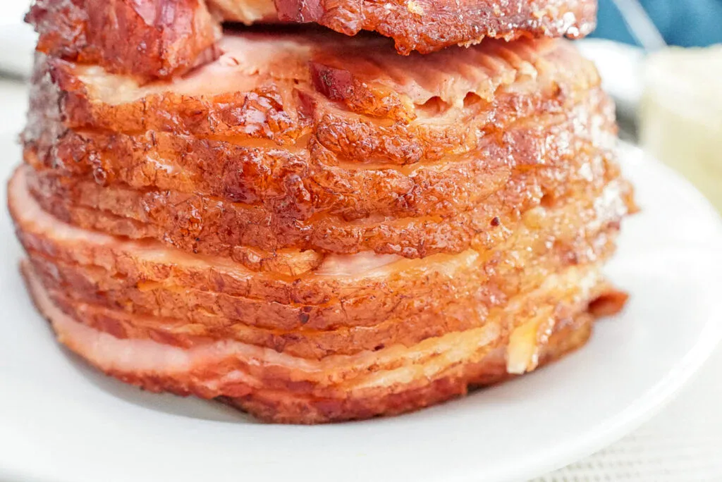 A close-up of sliced spiral ham stacked on a white plate.