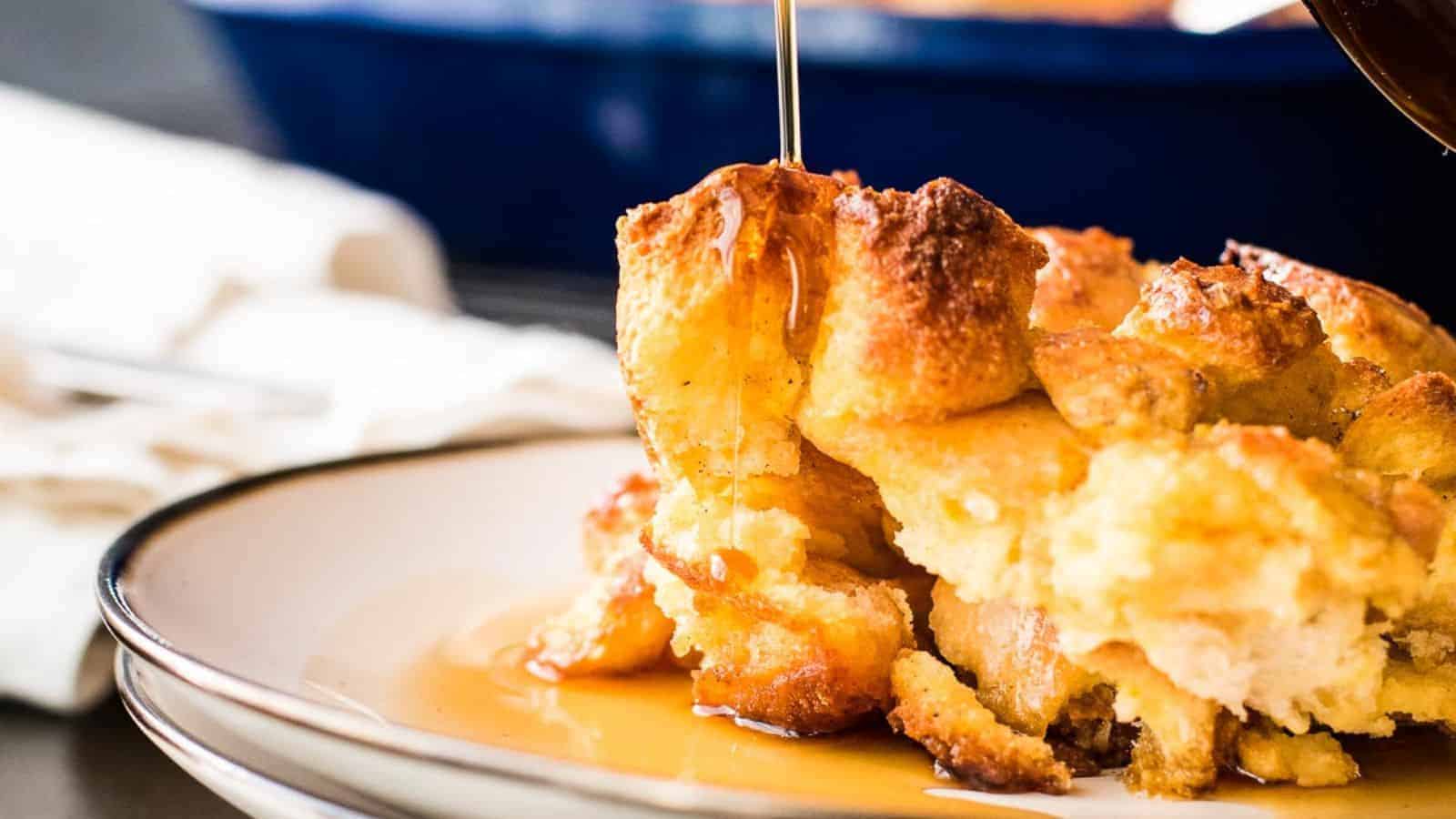A close-up of bread pudding on a plate with syrup being poured over the top.