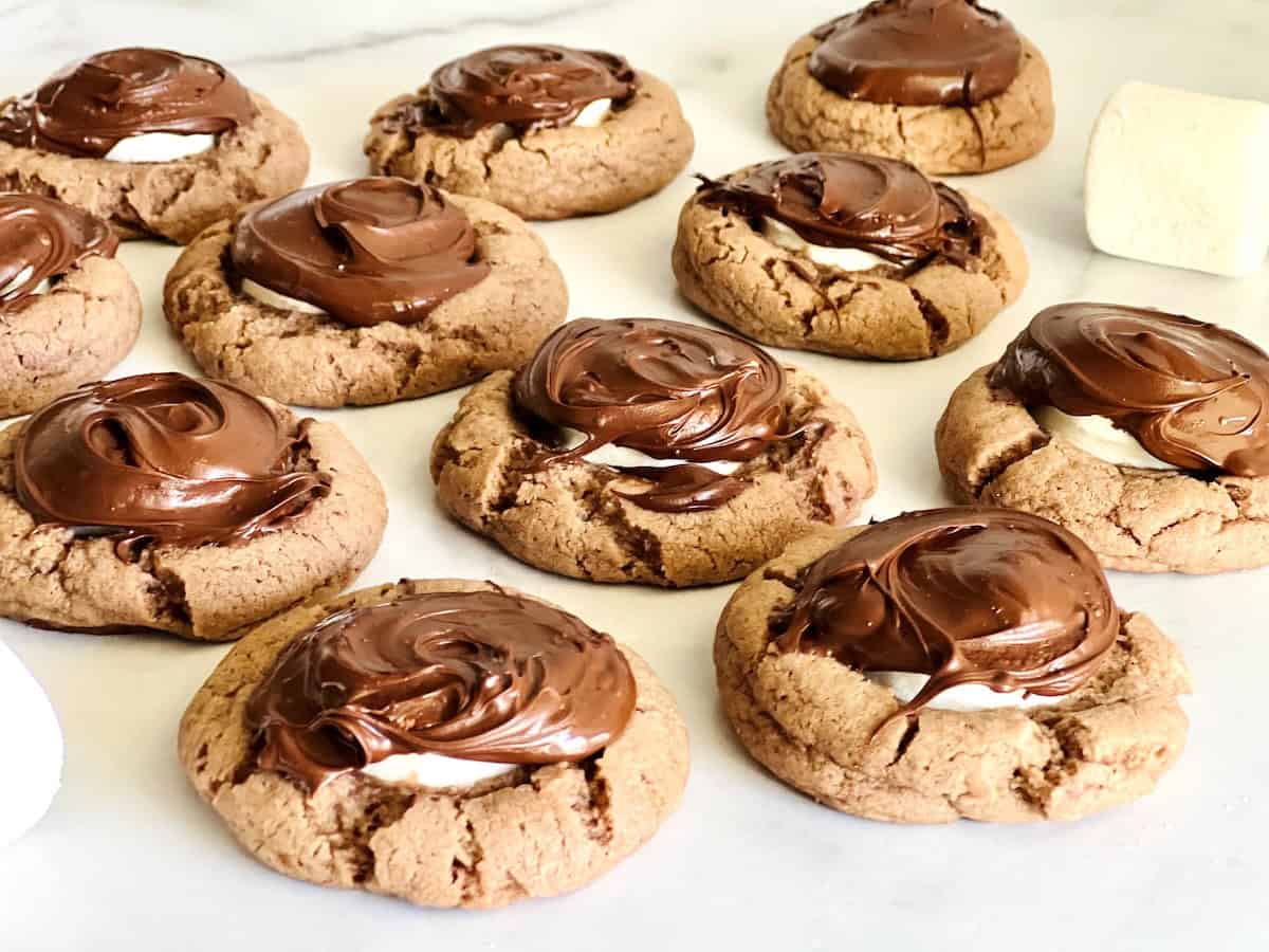 A batch of chocolate cookies topped with swirled chocolate and melted marshmallow, displayed on a white surface.