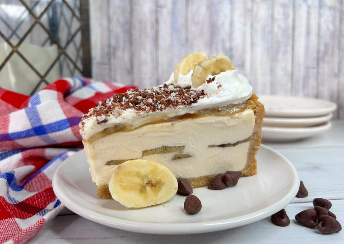 A slice of banana cream pie topped with whipped cream, chocolate shavings, and banana slices, served on a plate with chocolate chips.