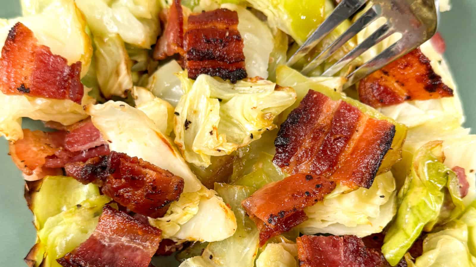Chopped cooked cabbage and crispy bacon pieces on a plate, with a fork resting on top.