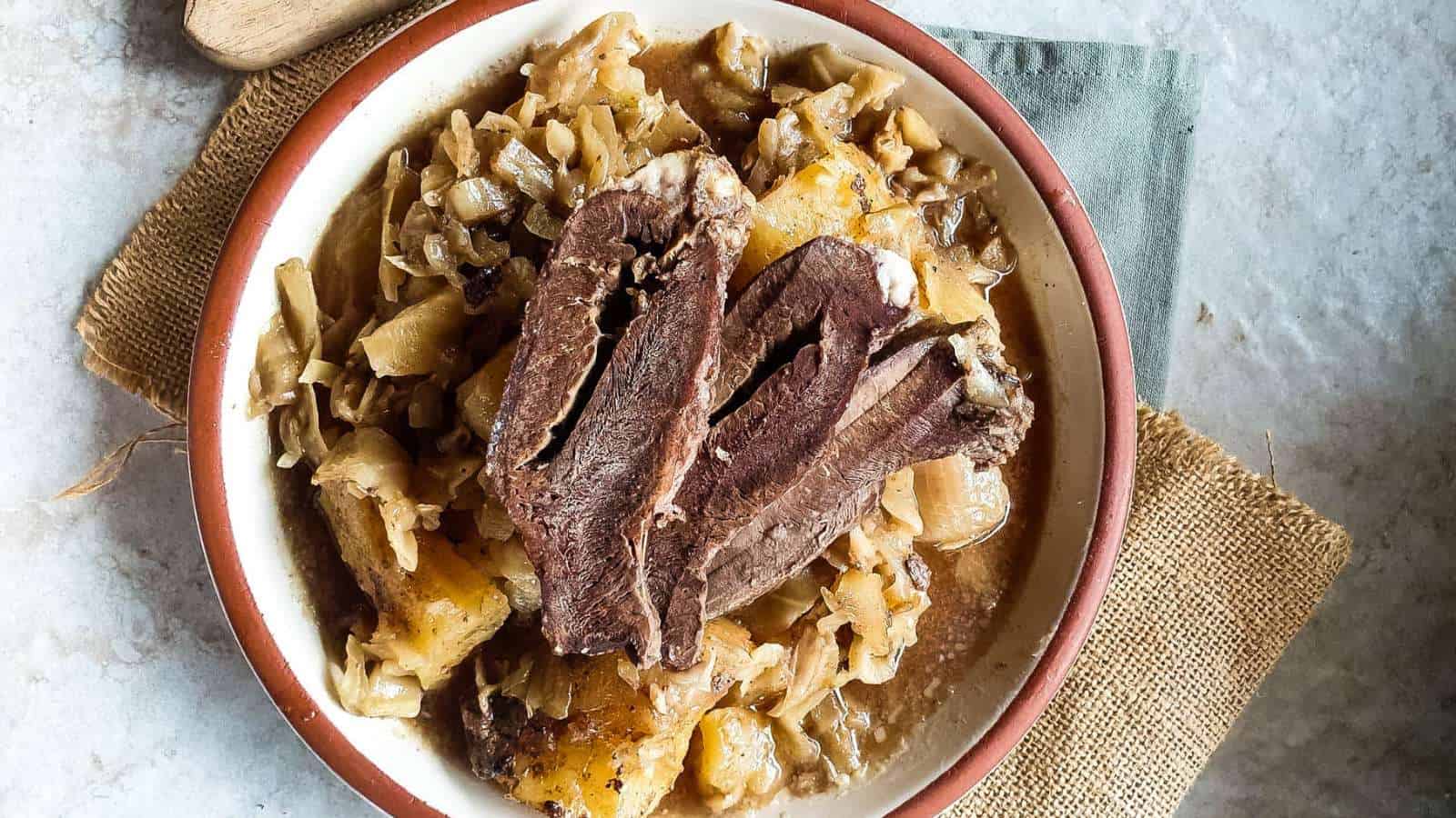 A bowl of cooked meat slices served over cabbage and potatoes on a rustic placemat.