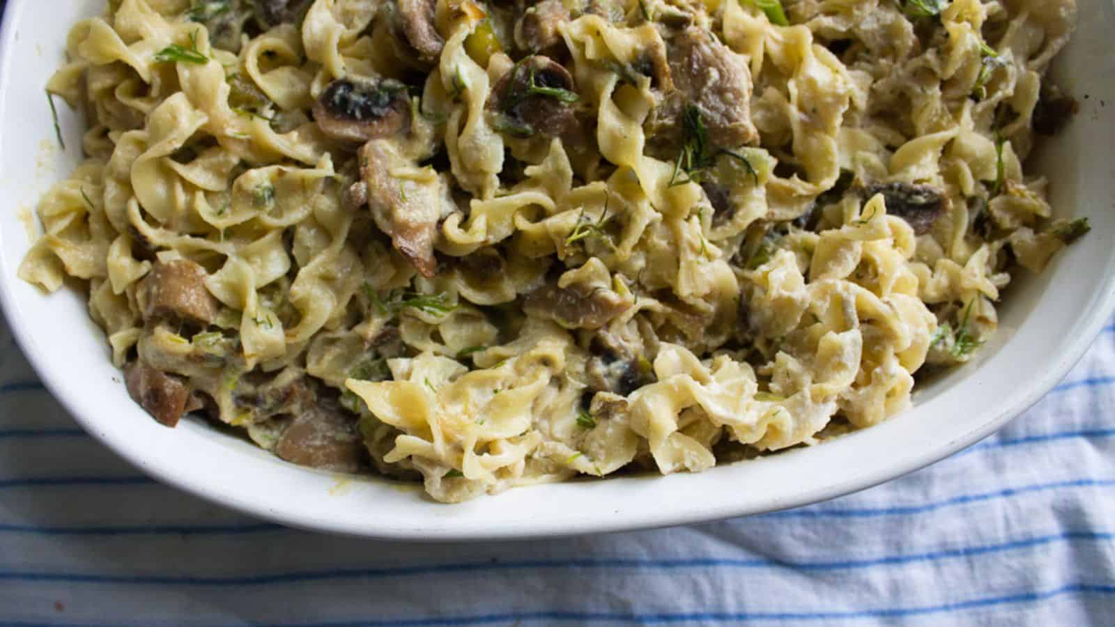 A white dish filled with creamy pasta mixed with mushrooms and herbs, placed on a blue and white striped cloth.