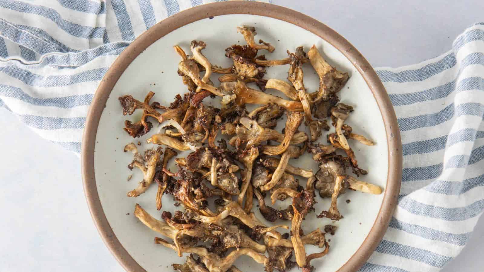 A plate of cooked, crispy mushrooms sits on a white dish with a brown rim, placed on a blue and white striped cloth.