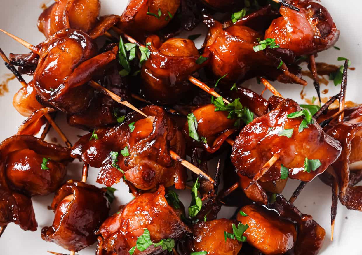 Barbecue-glazed bacon-wrapped chicken bites secured with toothpicks and garnished with chopped parsley on a white plate.