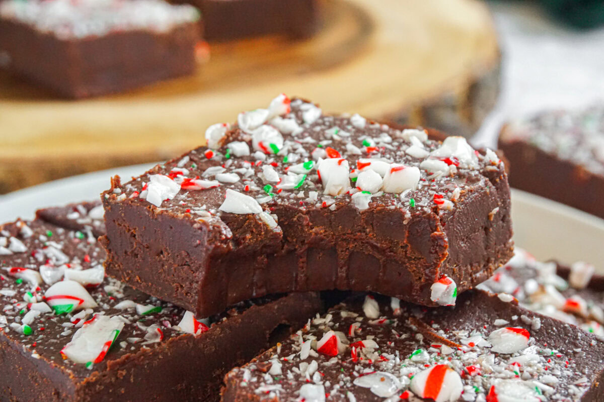 Close-up of chocolate fudge squares topped with crushed peppermint candy, with one piece showing a bite taken out.