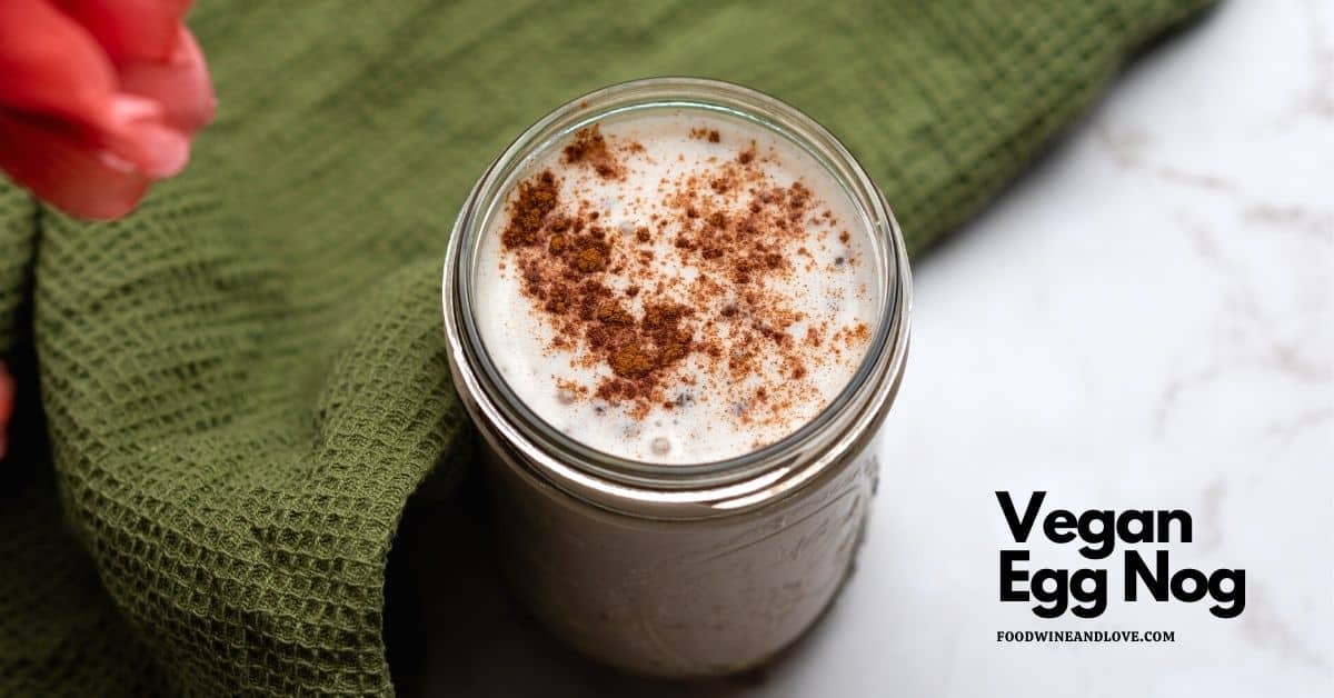 A glass jar filled with vegan egg nog topped with cinnamon, placed on a green cloth with text reading Vegan Egg Nog.