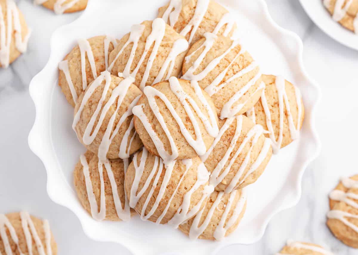 A plate of round cookies with white icing drizzled on top, arranged in a neat stack on a white scalloped dish.