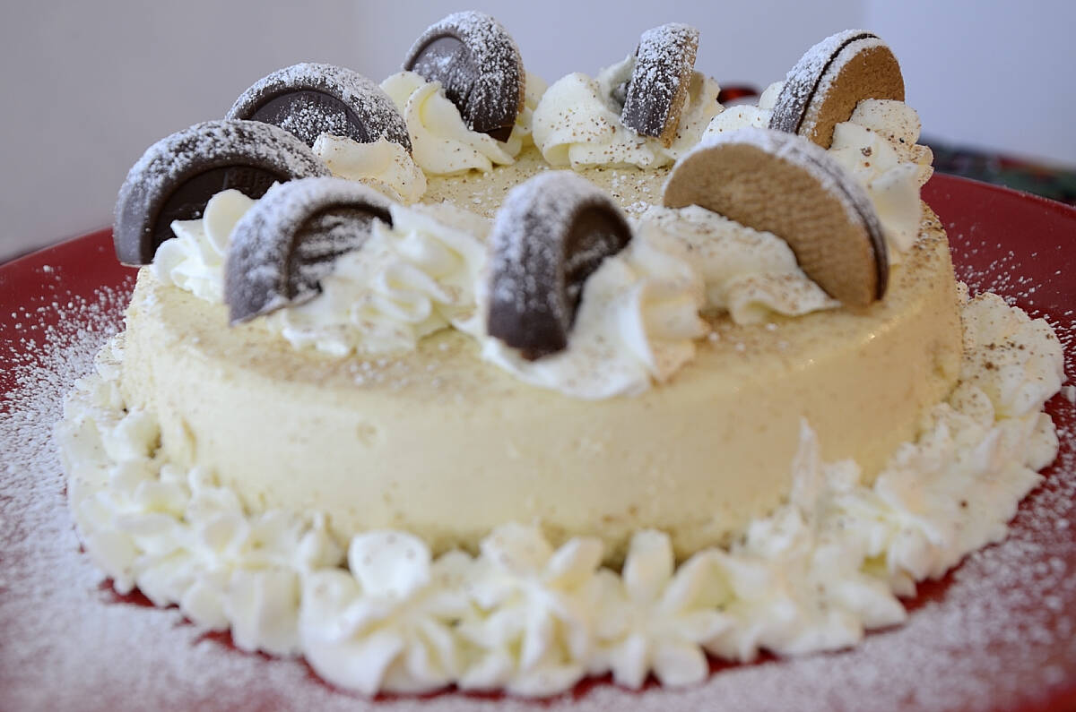 Round cake topped with whipped cream, chocolate cookies, and dusted with powdered sugar, displayed on a red plate.