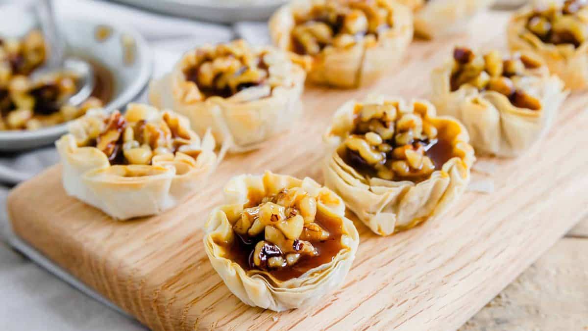 Mini phyllo pastry cups filled with caramelized nuts arranged on a wooden serving board.