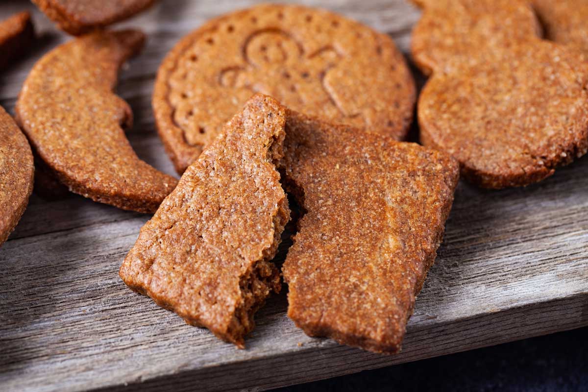 A close-up of spiced cookies on a wooden surface, including a gingerbread cookie and a rectangular cookie broken in half.