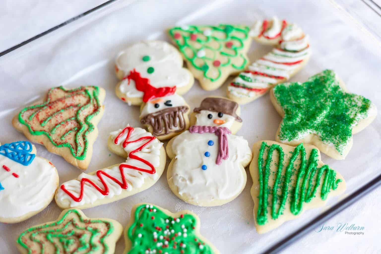 A tray of assorted Christmas-themed sugar cookies decorated with colorful icing, featuring snowmen, trees, and candy cane shapes.