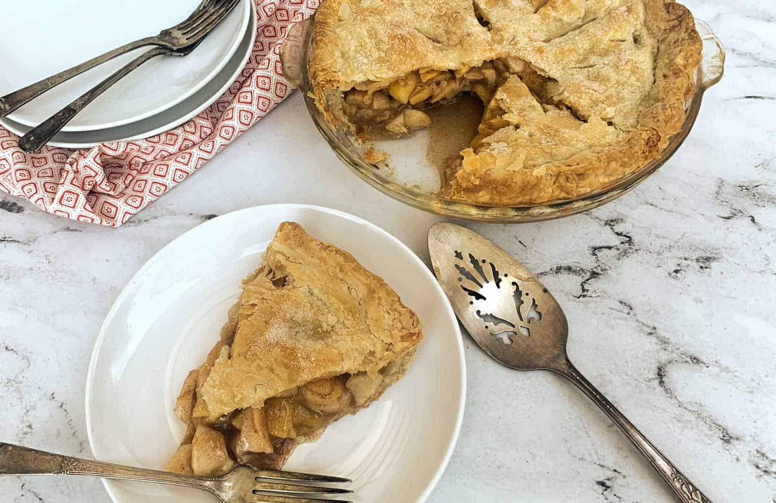 Apple pie with a lattice crust on a marble surface, one slice on a