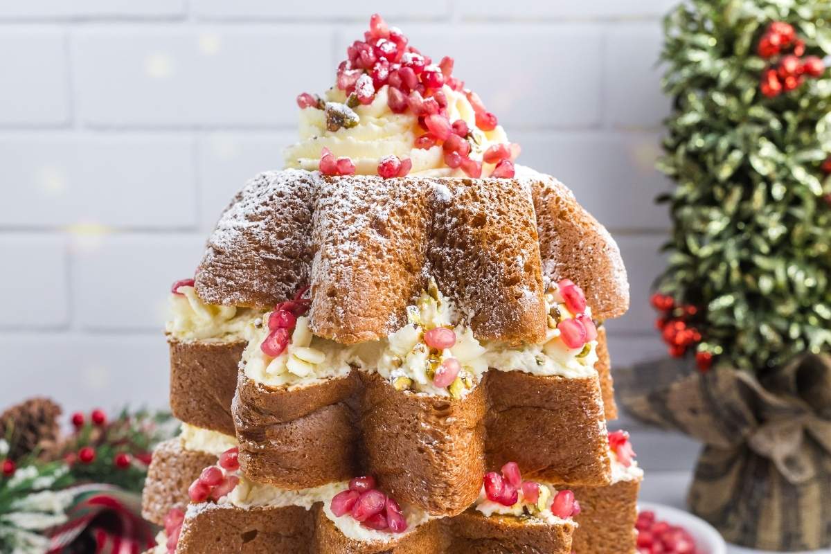 A layered star-shaped cake dusted with powdered sugar, filled with cream, and topped with pomegranate seeds, set on a festive table.