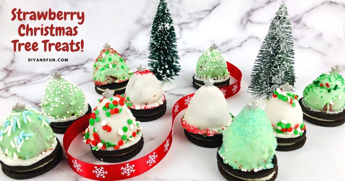 Decorated strawberry Christmas tree treats covered in white and green icing, placed on Oreo cookies, with small Christmas trees and a red ribbon in the background.