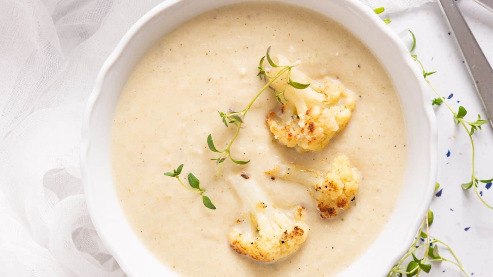 A bowl of creamy cauliflower soup garnished with roasted cauliflower florets and fresh thyme.