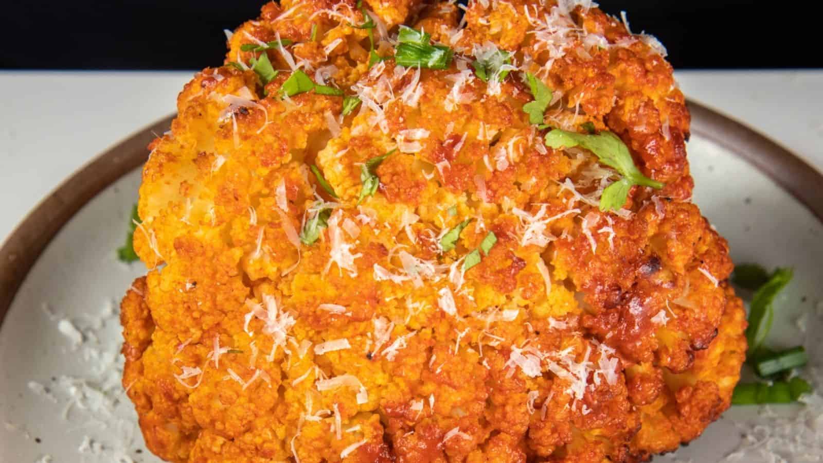 Whole roasted cauliflower topped with grated cheese and herbs, served on a plate.