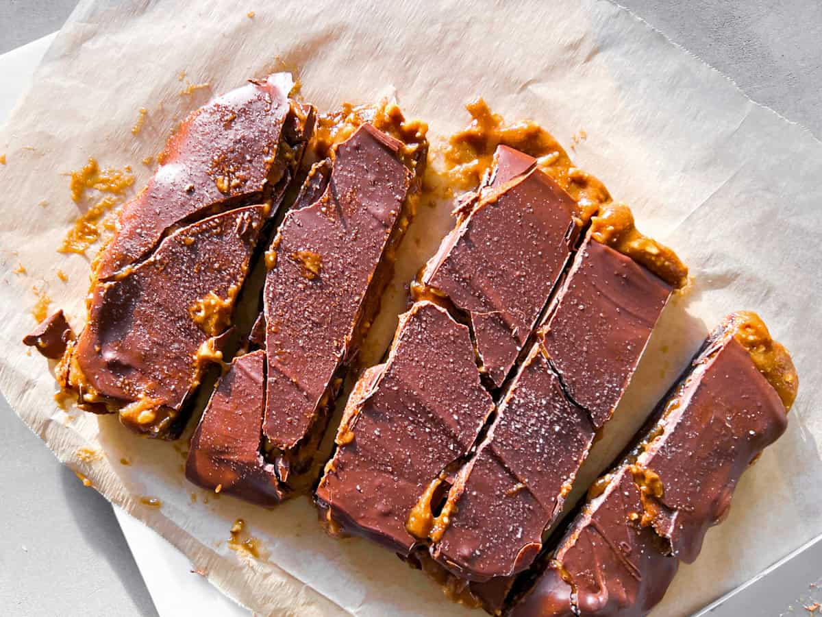 Five chocolate-covered caramel bars are arranged on parchment paper, with visible caramel oozing out from the sides and a sprinkling of salt on top.