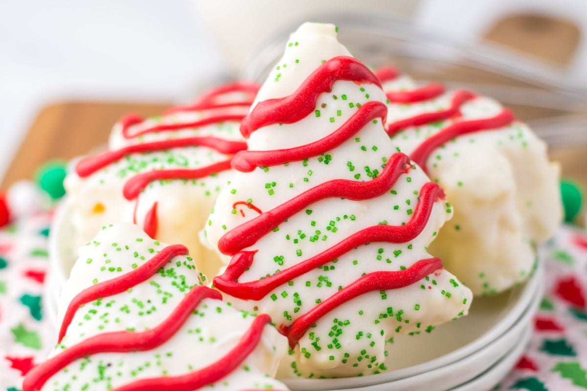 Christmas tree-shaped cookies with white icing, red frosting decorations, and green sprinkles on a plate.