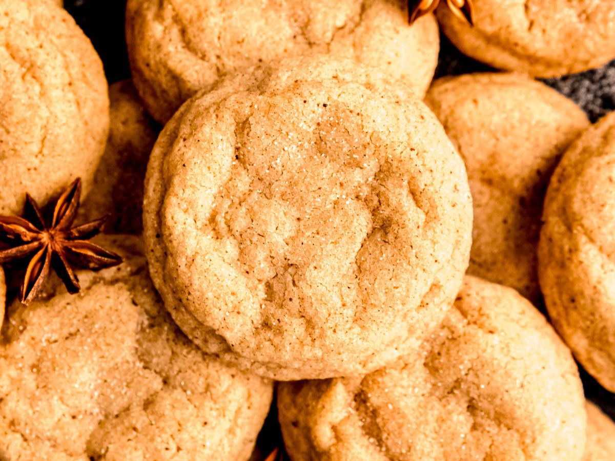Close-up of several round, golden-brown cookies with a sugar coating, arranged together with a few star anise pods visible.