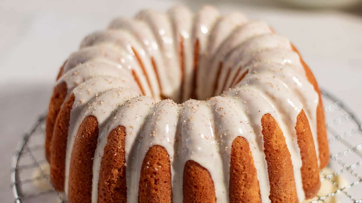 A bundt cake topped with white icing sits on a cooling rack.