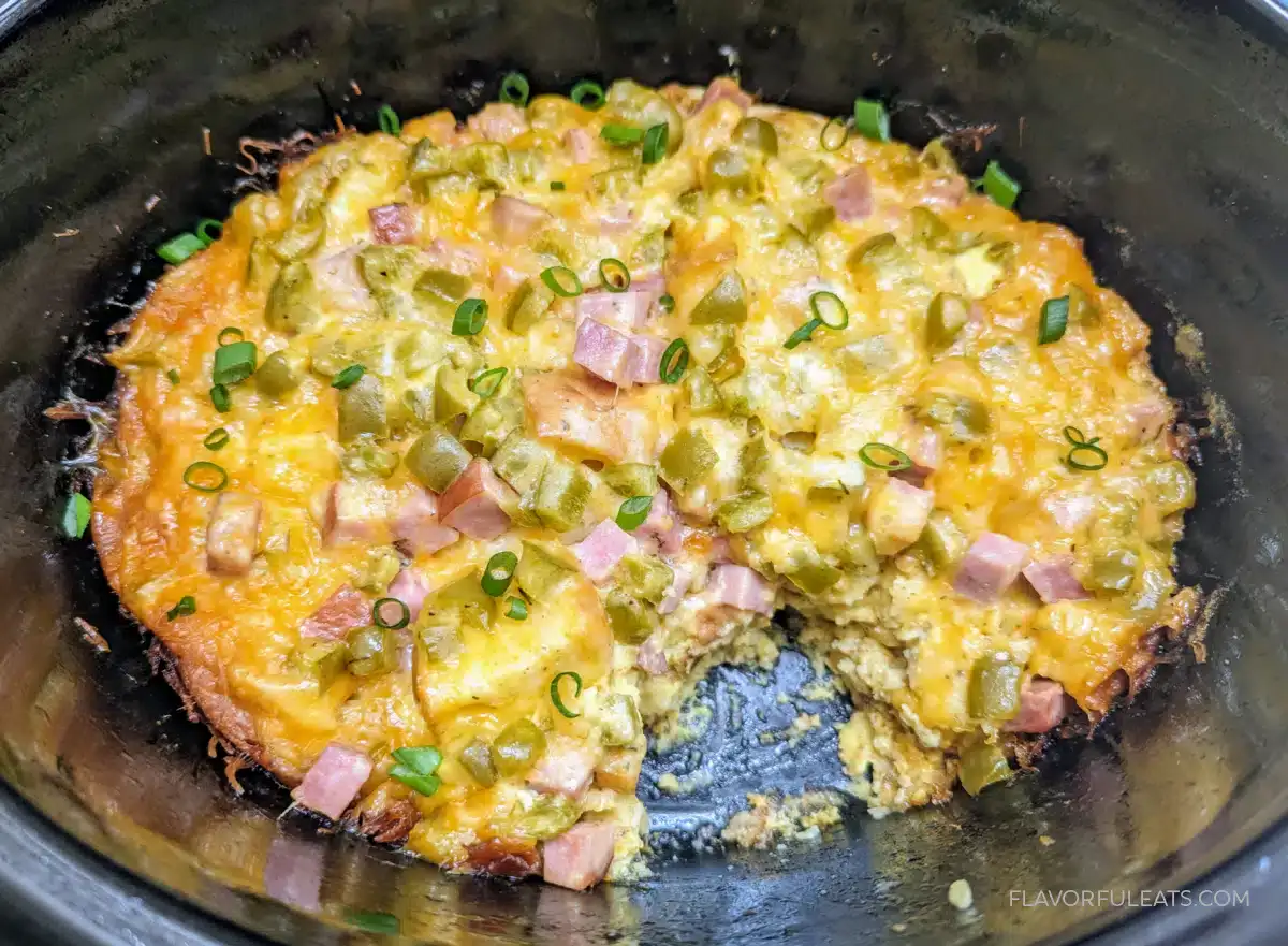 Casserole with melted cheese, diced ham, green chiles, and chopped green onions, partially served in a black dish.