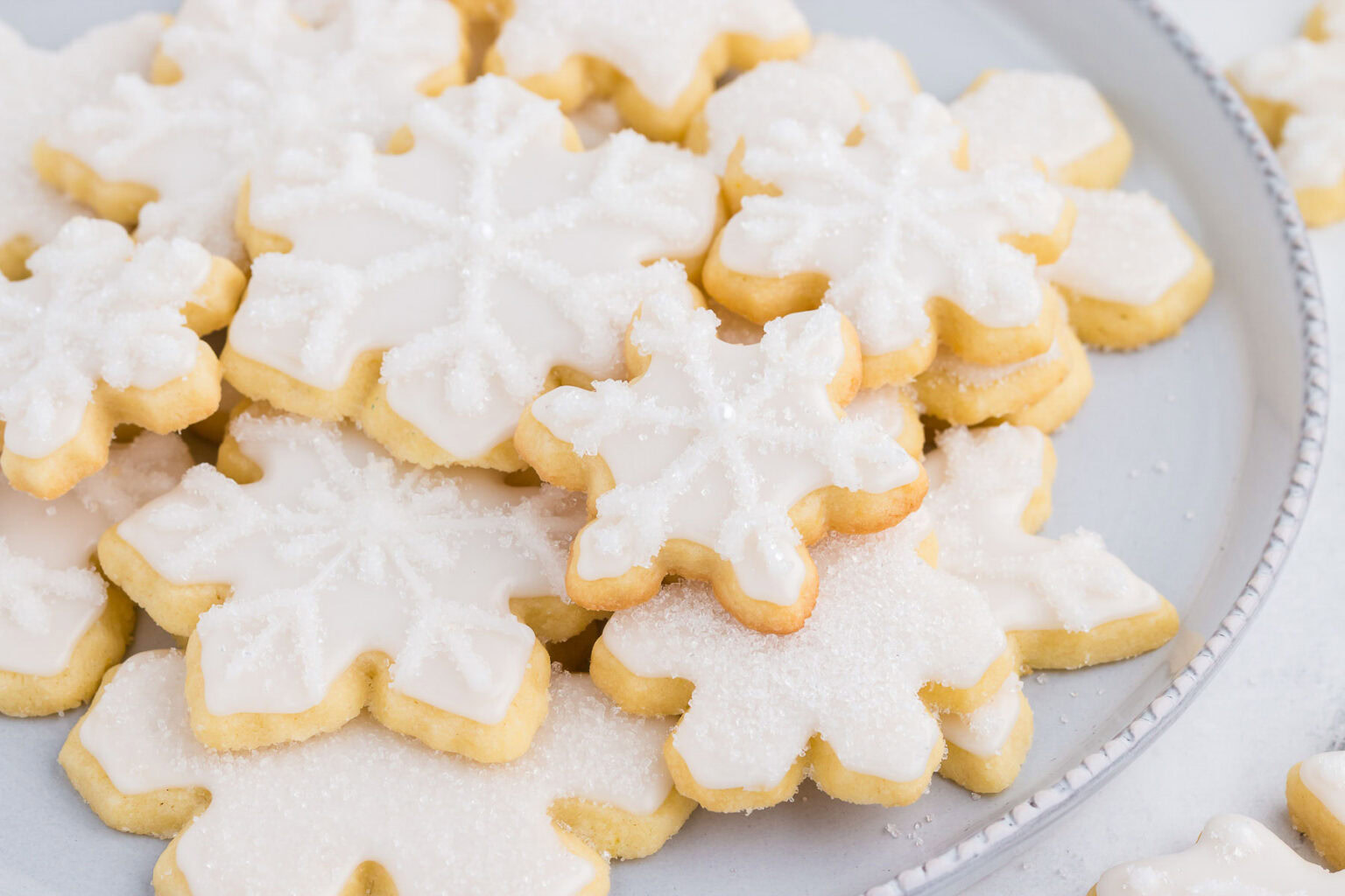 A plate of snowflake-shaped sugar cookies decorated with white icing and sugar crystals.