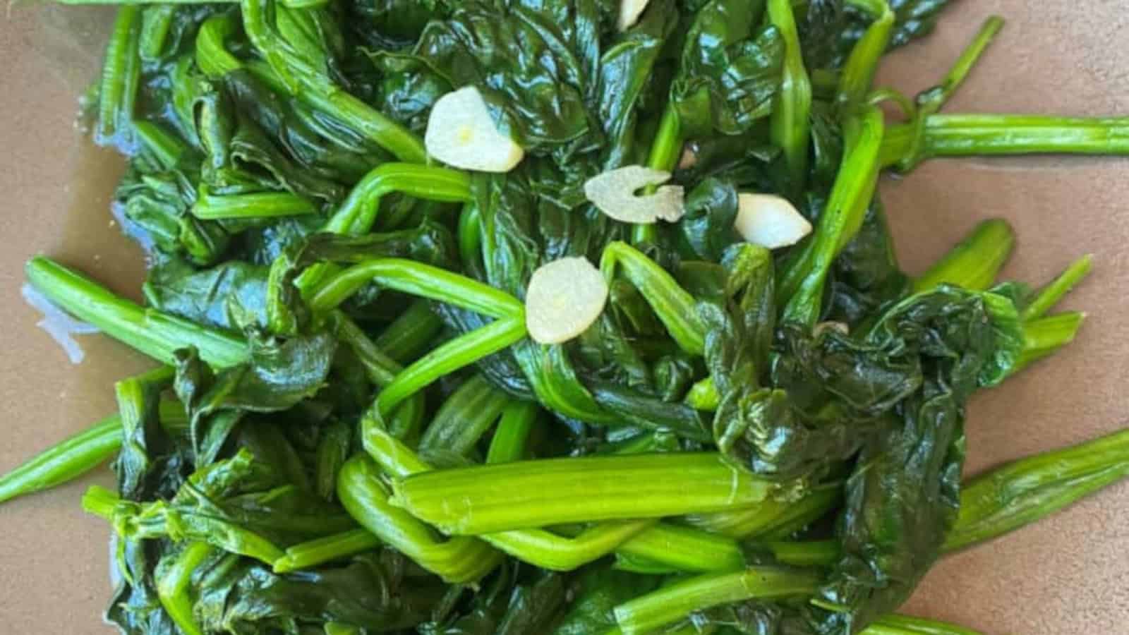 A plate of sautรฉed water spinach with sliced garlic pieces.