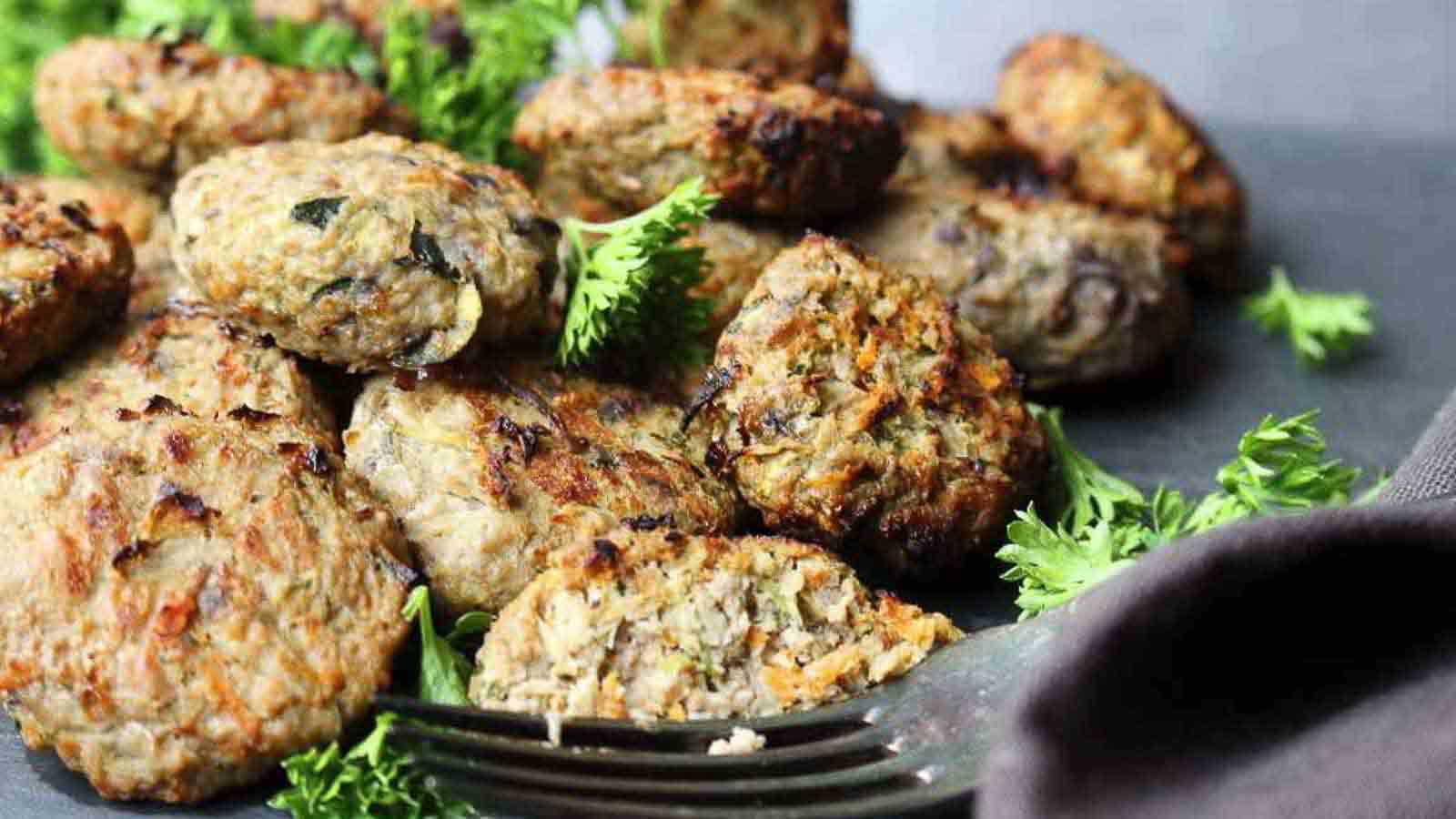A close-up of several cooked meat patties on a dark surface, garnished with fresh parsley, with a fork in the foreground.