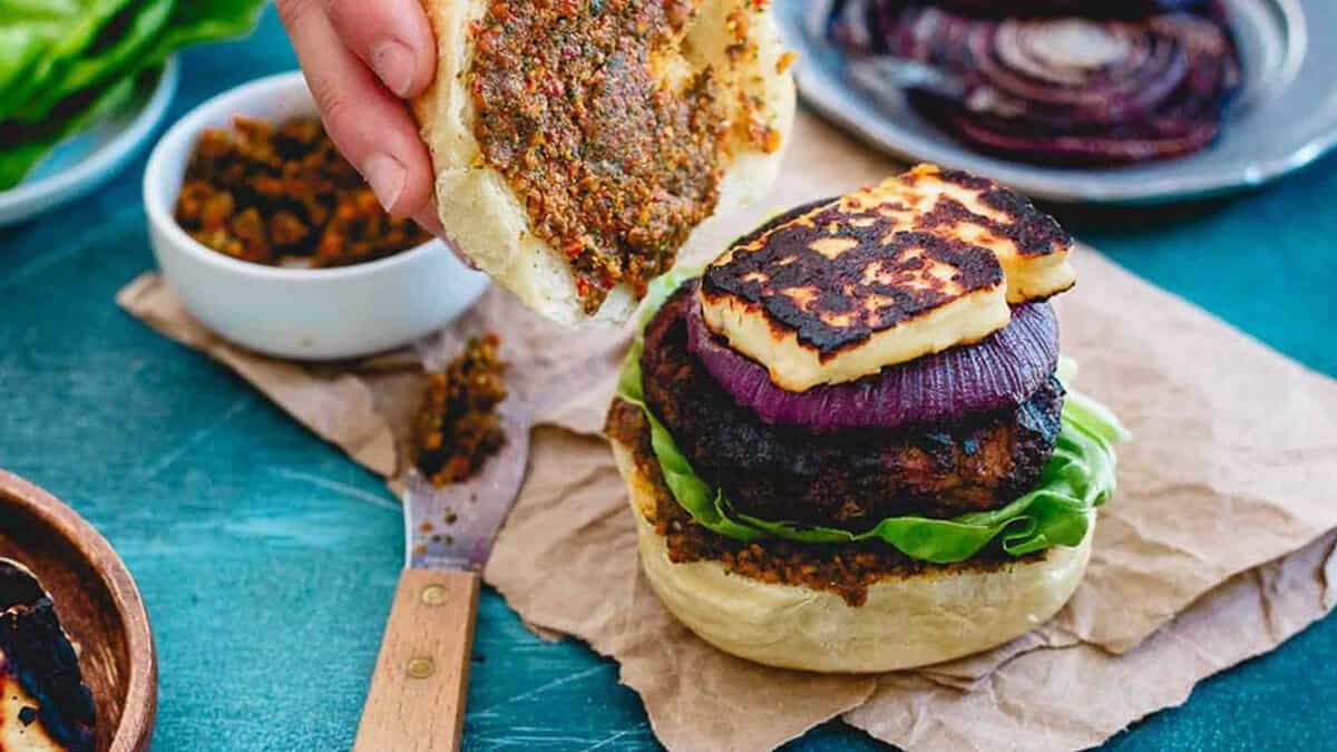 A burger bun topped with lettuce, a grilled patty, a slice of grilled onion, and grilled halloumi cheese, with the top bun being spread with sauce.