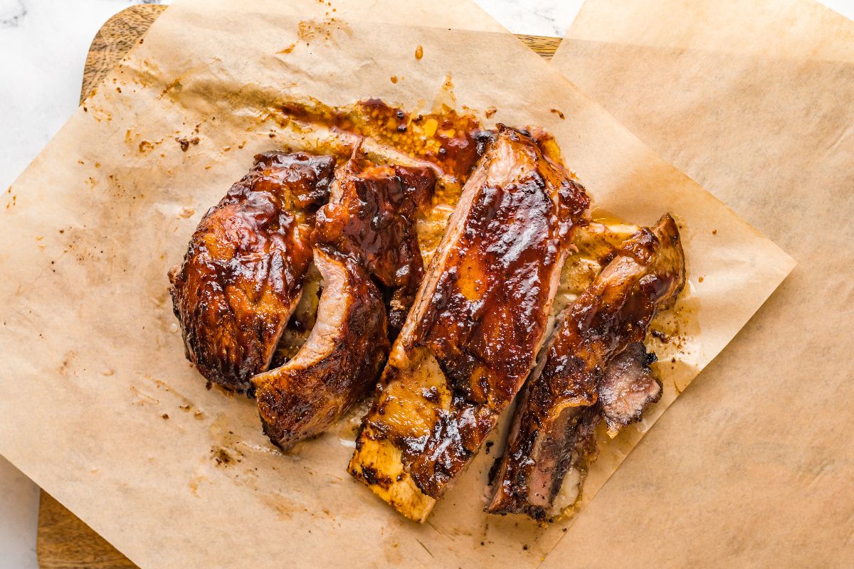 Three pieces of barbecued ribs with a glazed, caramelized surface are placed on a sheet of brown parchment paper.