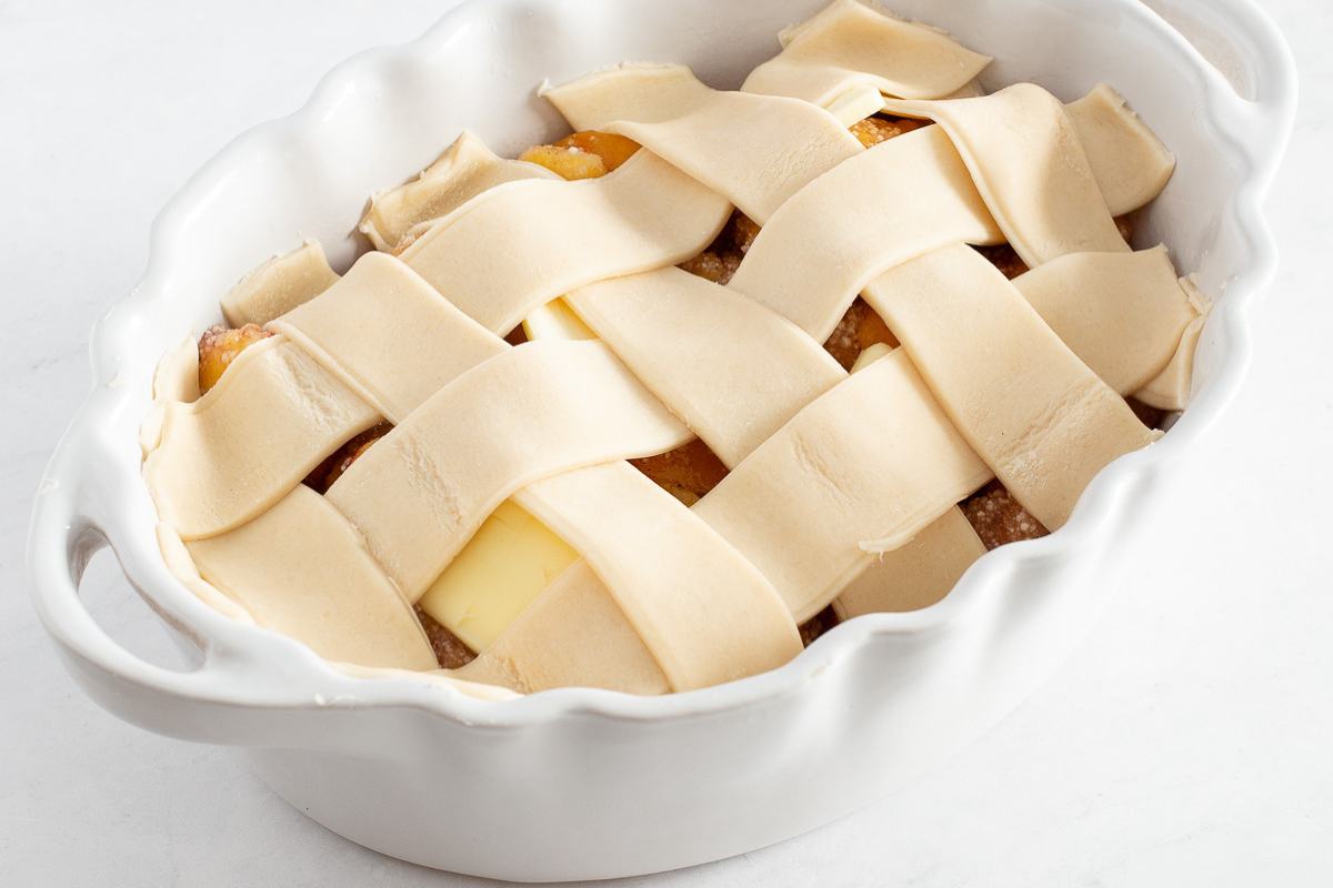 Unbaked pie in a white dish with a lattice crust and visible piece of butter inside.
