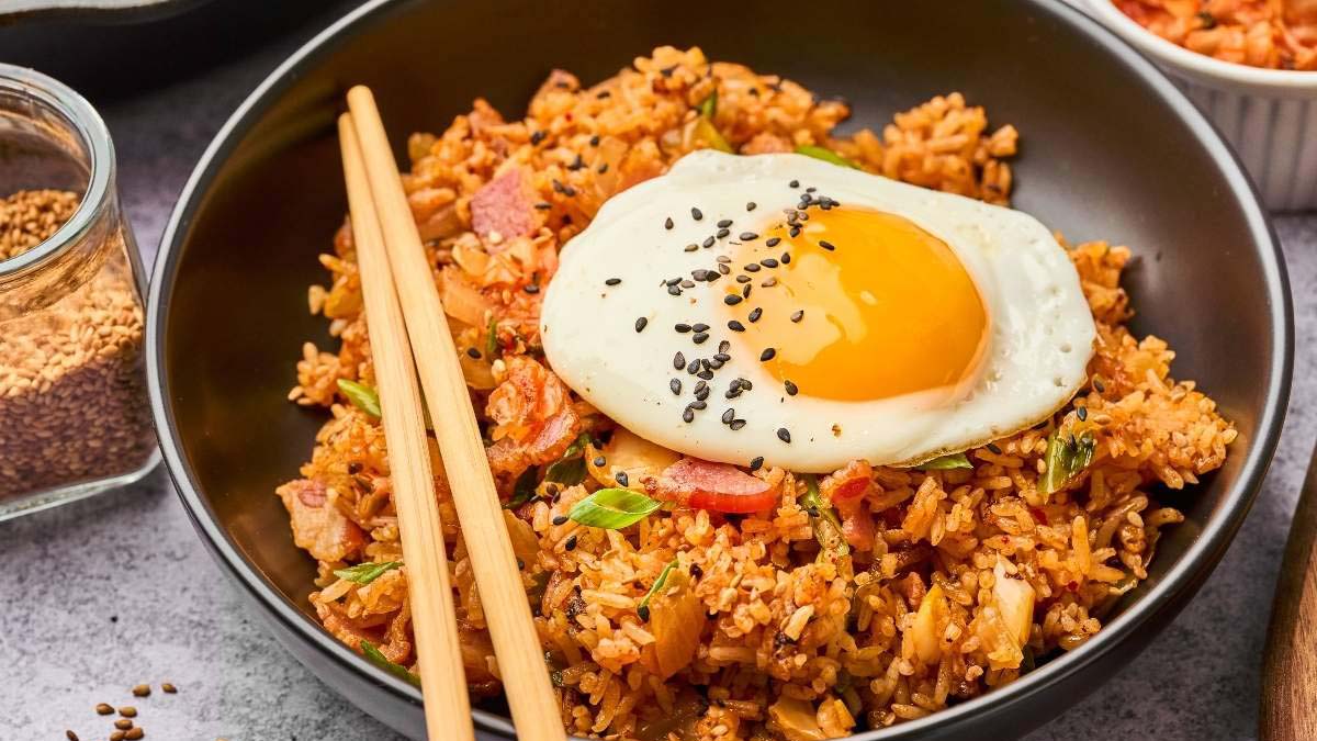 A bowl of kimchi fried rice topped with a sunny-side-up egg and black sesame seeds, with chopsticks resting on the bowl.