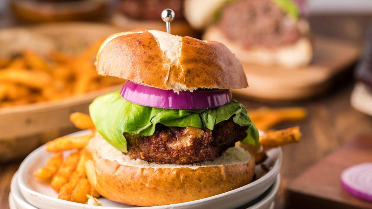 A hamburger with lettuce and a slice of red onion on a bun, served with French fries on a white plate.