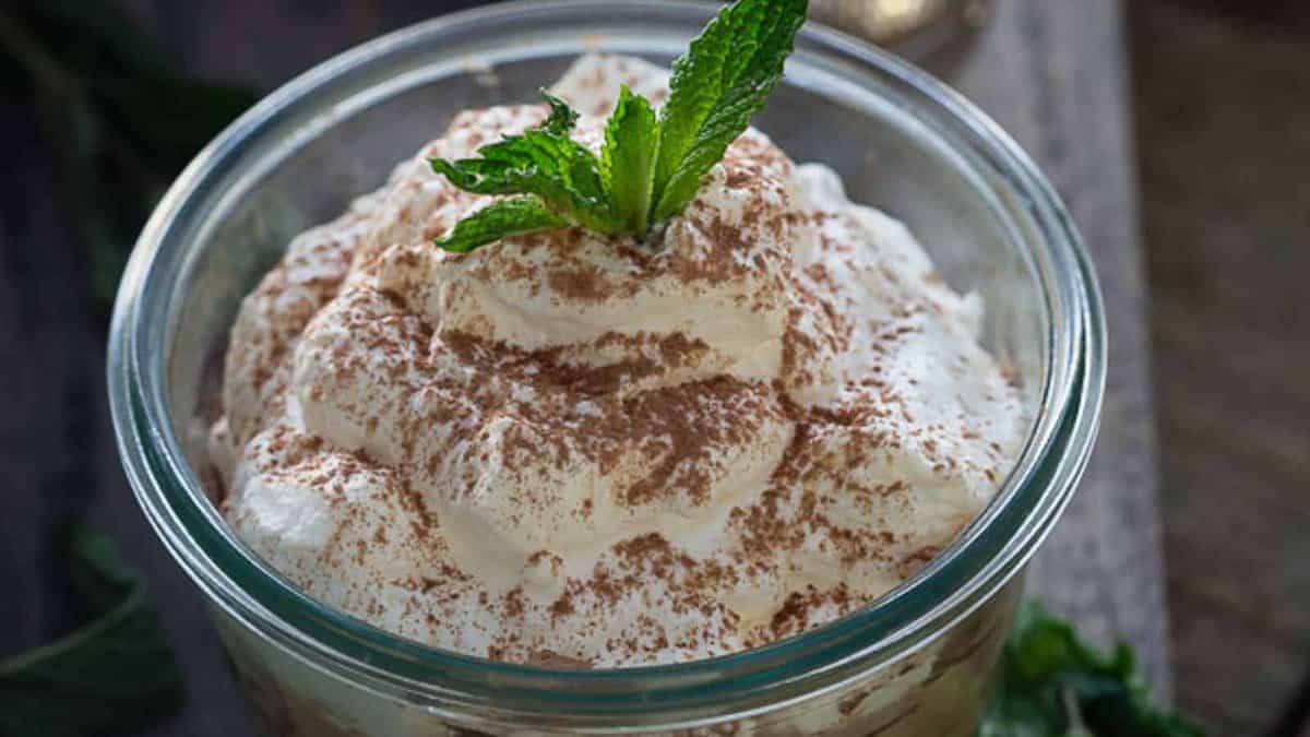 A glass bowl filled with whipped cream topped with cocoa powder and a sprig of fresh mint.