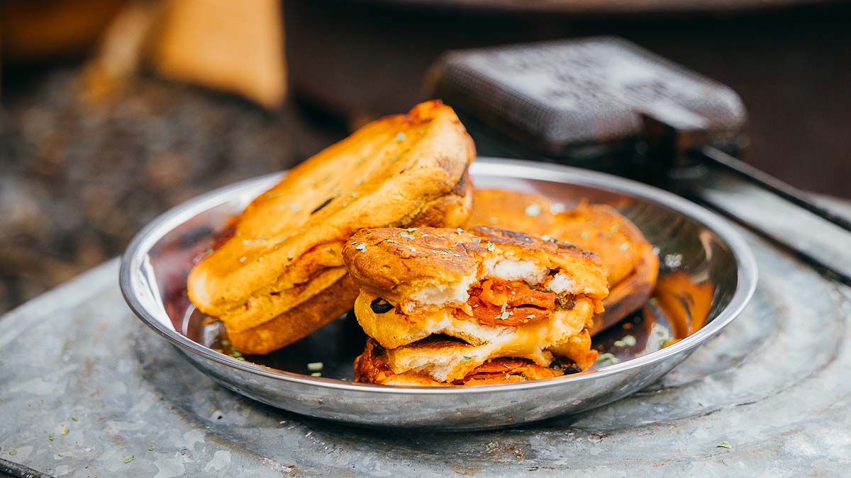 A metal plate holding several toasted sandwiches filled with melted cheese and pepperoni, with one sandwich split open to show the filling.