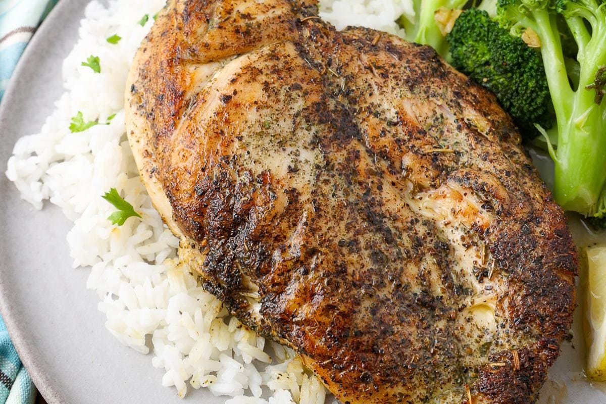 A seasoned, grilled chicken breast served on white rice with steamed broccoli on the side.