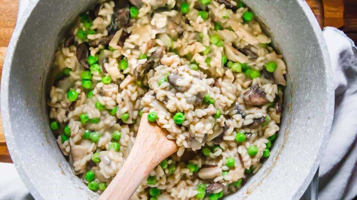 A pot of mushroom and pea risotto being stirred with a wooden spoon.