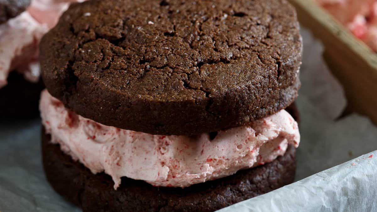 A chocolate ice cream sandwich with pink strawberry ice cream filling, placed on parchment paper.